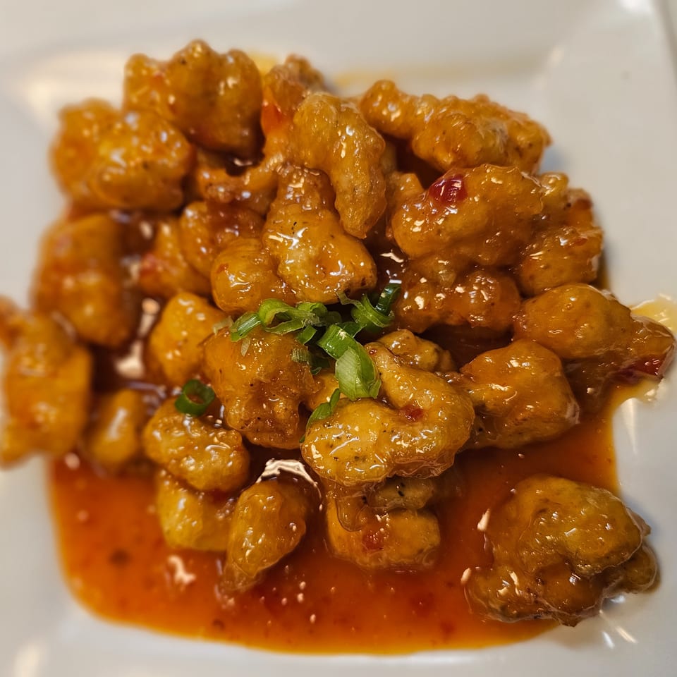 Crispy golden cauliflower florets coated in glossy orange sauce and garnished with sliced green onions on a white plate.
