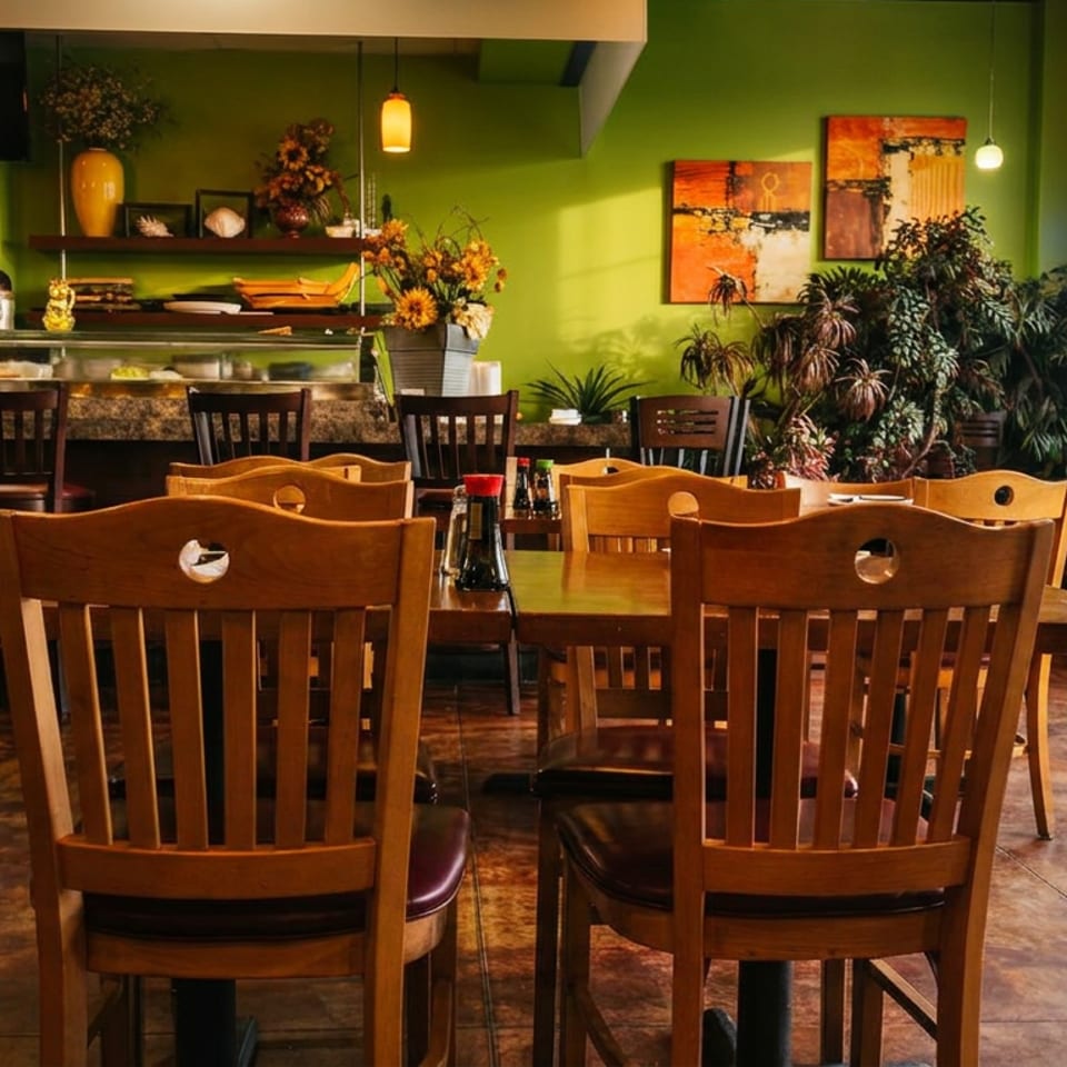 Empty dining room of a restaurant with wooden tables and chairs, green walls, and a sushi bar.