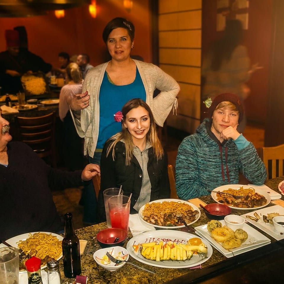 A family of four enjoying a meal together at a hibachi restaurant, with plates of food on the table.